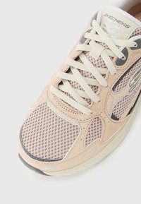 Baskets Skechers beige et blanches avec tissu en maille, accents en daim, lacets crème et languette de marque sur fond blanc.