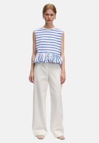 Blauw-wit gestreepte mouwloze top met een gerimpelde zoom, gecombineerd met hoge witte culottebroeken en lichte schoenen.