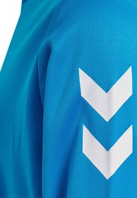 Blå sportskjorta med texturerad tyg, med tre vita chevrons placerade på ärmen.