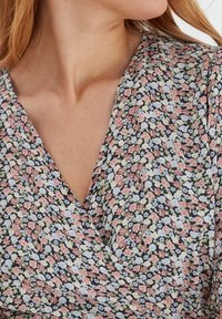 Top de envoltura floral con escote en V, que presenta un fondo oscuro y pequeñas flores multicolores en rosa, azul y verde. Textura de tela suave.