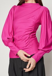 Tajta långärmad topp i klar rosa, med rynkdetalj på sidan, hög halsringning och voluminösa ärmar med elastiska muddar.