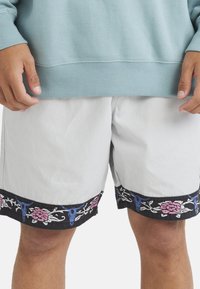 Person wearing light blue sweatshirt and white shorts with black trim featuring blue and pink floral patterns.