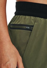 Olivgrön träningsbyxor med svart elastiskt midjeband, utrustade med en dragkedjeficka på sidan och en slät, texturerad tyg.