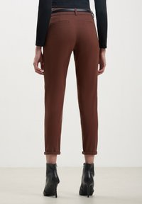 Pantaloni brown a sigaretta con risvolti, tasche posteriori, abbinati a stivaletti neri alla caviglia. Materiale liscio con una finitura elegante.