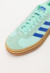 Ljus myntgrön sneakers med blåa ränder, i ett material av mocka och syntet, gummisulor och texturerade detaljer på tungan.