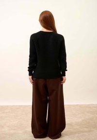 Czarny dzianinowy sweter z okrągłym dekoltem, w połączeniu z szerokimi brązowymi spodniami. Sweter ma prążkowane mankiety i dół. Miękka, fakturowana tkanina.