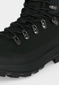 Črni pohodniški čevelj z robustnim podplatom, kovinskimi zankami za vezalke, okroglimi črnimi vezalkami in nepremočljivim Gore-Tex materialom.