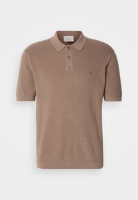 Polo tričko s krátkym rukávom vo svetlohnedej farbe, vyrobené z štruktúrovanej tkaniny. Obsahuje klasický golier a uzáver so 3 gombíkmi. Vyšívané logo CK.