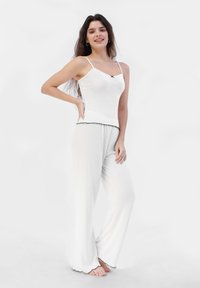 Top blanco sin mangas con tirantes ajustables y detalles en negro, combinado con pantalones blancos sueltos que presentan un dobladillo con forma de scallop. Tejido suave y ligero.