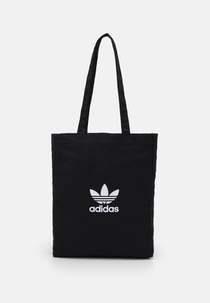 Czarna torba typu tote marki Adidas z długimi uchwytami oraz białym logo trefoil umieszczonym centralnie na froncie na jednolitym tle.