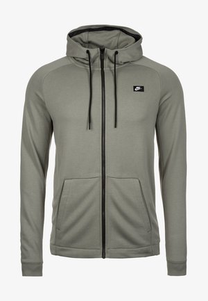 Hellgraue Nike-Kapuzensweatjacke mit durchgehendem Reißverschluss, schwarzen Kordeln, vorderen Kängurutaschen und einem kleinen schwarzen Nike-Logo-Patch auf der linken Brust.