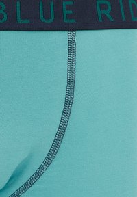 Bolečki iz svetlo modrega blaga imajo mornarsko elastično obod, na katerem je napisan tekst "BLUE RIDGE", gladko teksturo in kontrastne šive.