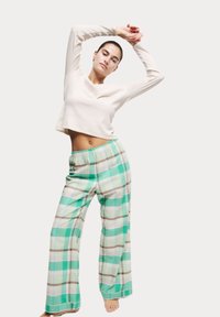 Crème kleurige blouse met lange mouwen en een ronde halslijn, gecombineerd met lichtgroene geruite pyjamabroek met een losse pasvorm en een elastische tailleband.