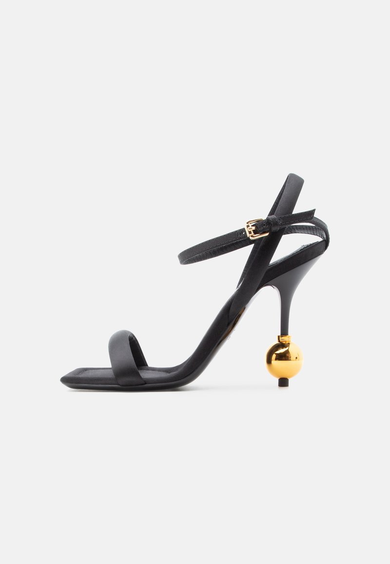 Μαύρο σανδάλι με ψηλό τακούνι, λεπτό λουράκι στον αστράγαλο και μοναδική χρυσή σφαιρική λεπτομέρεια στο τακούνι, με τετράγωνη μύτη.