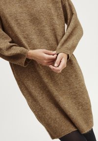 Abito lavorato a maglia marrone con una vestibilità ampia, maniche lunghe e polsini a costine. Texture morbida con un motivo sottile. I bordi sono leggermente affusolati.