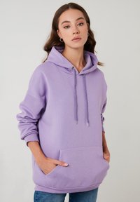 Sudadera oversized de color púrpura hecha de una tela suave, con capucha ajustable, bolsillo frontal y puños de canalé. Textura suave y diseño casual.