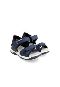 Marineblaue Sandalen mit verstellbaren Klettverschlüssen, weißen Gummisohlen und gepolstertem Innenfutter. Merkmale sind Aussparungen für Atmungsaktivität.