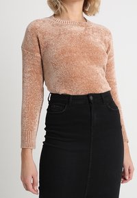 Gebreide trui in licht terracotta met een ronde halslijn en geribde manchetten, gecombineerd met een zwarte denim pencil skirt met een split aan de voorkant.