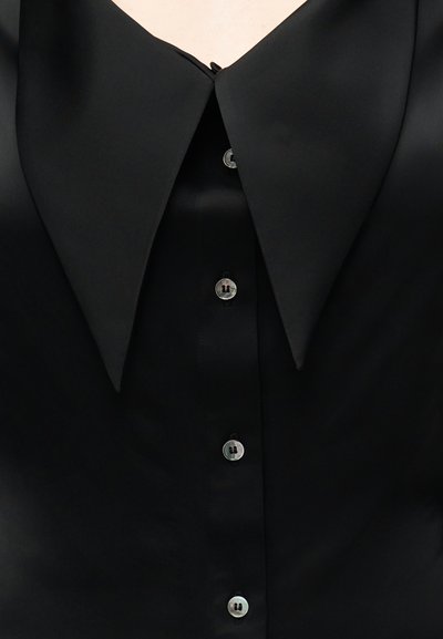 Μαύρο πουκάμισο με υπερμεγέθη μυτερό γιακά και τέσσερα ορατά γυαλιστερά κουμπιά στο μπροστινό μέρος.