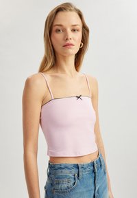 Lyserød crop top lavet af glat stof med tynde stropper, med en sort betonet udskæring og en lille sløjfedetalje i midten.