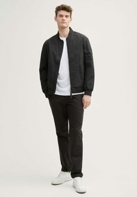 Chaqueta bomber negra con puños acanalados, camiseta blanca, pantalones negros y zapatillas blancas. Textura suave y diseño sencillo.
