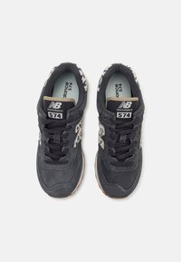 Paire de baskets noires New Balance 574 avec des accents imprimé léopard sur les côtés et la doublure intérieure, vue de dessus.