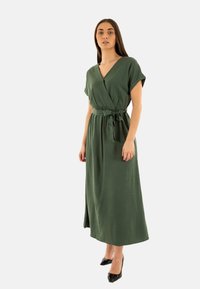 Vestido envolvente verde de tejido ligero, con mangas cortas, un lazo en la cintura y una falda larga con una abertura lateral.