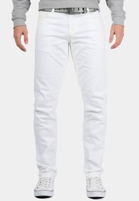 Jean en denim blanc avec des coutures jaunes, design slim fit et construction à cinq poches, associés à des baskets blanches et un sweat-shirt gris.