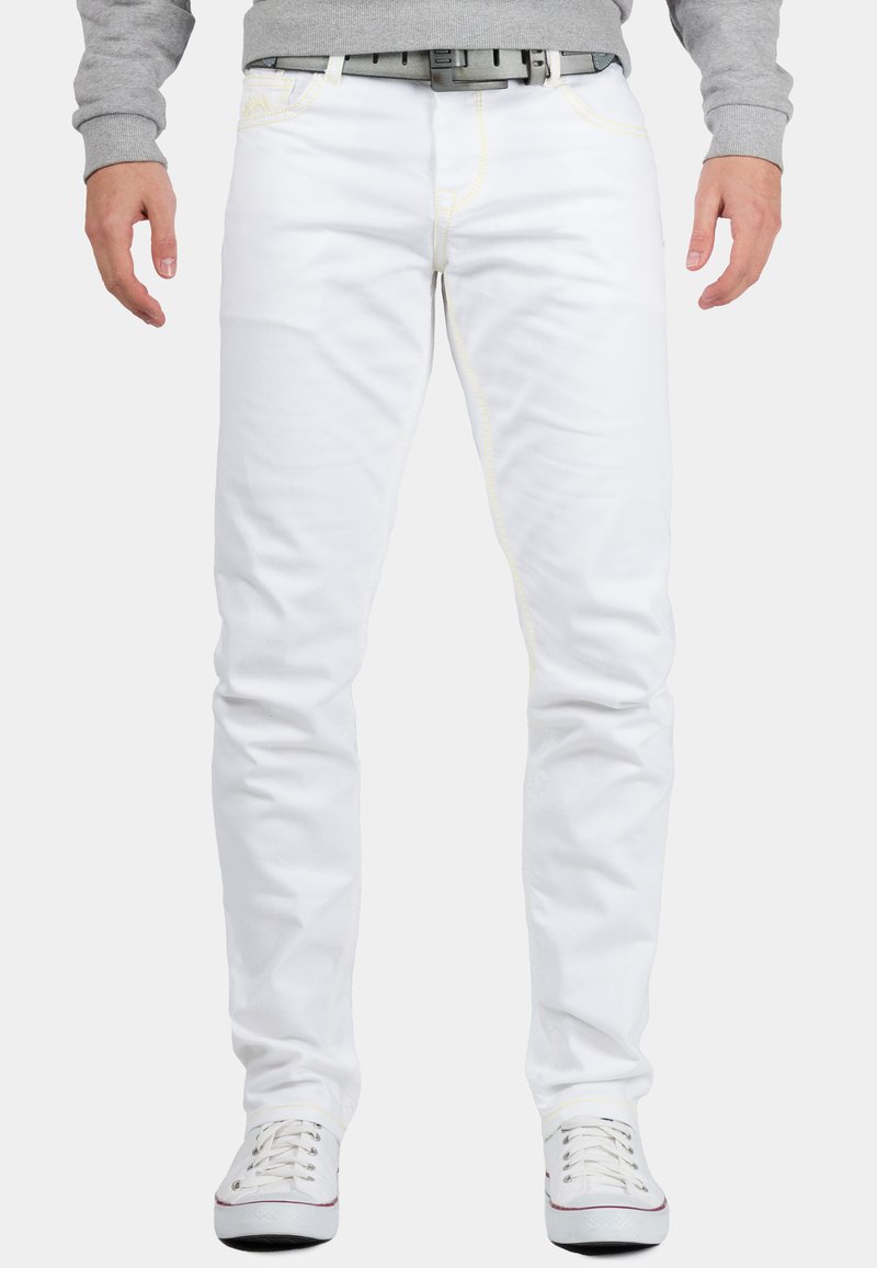 Jean en denim blanc avec des coutures jaunes, design slim fit et construction à cinq poches, associés à des baskets blanches et un sweat-shirt gris.