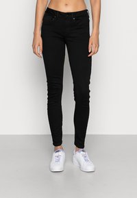 Jean skinny noir en denim avec cinq poches, une braguette à boutons et des passants pour ceinture, associé à des baskets blanches avec des accents violets.