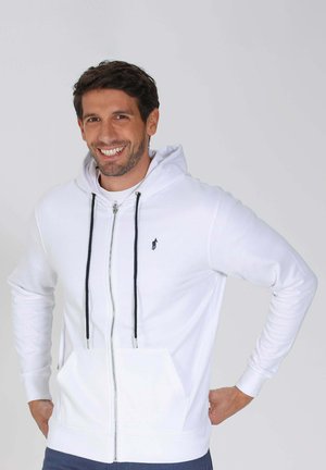 Sweat à zip blanc avec capuche, cordons de serrage noirs, poches kangourou et un petit logo sur la poitrine gauche. Tissu doux en mélange de coton.