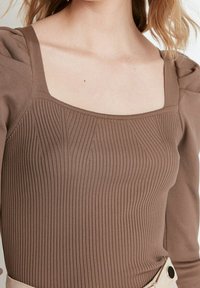 Brauner gerippter Body mit quadratischem Ausschnitt und gepufften Schultern. Der Stoff ist weich, hat eine figurbetonte Passform und dezente Strukturdetails.