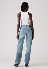 Jeans in denim azzurro chiaro con vestibilità comoda, caratterizzati da cuciture evidenti, stile a cinque tasche e una patch in pelle marrone sulla cintura posteriore.