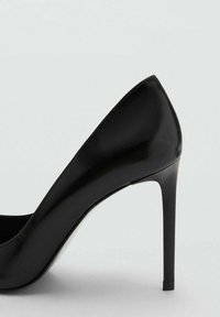 Zapato de tacón alto de cuero negro con puntera afilada y una silueta elegante, que presenta una textura suave y un tacón de aguja.