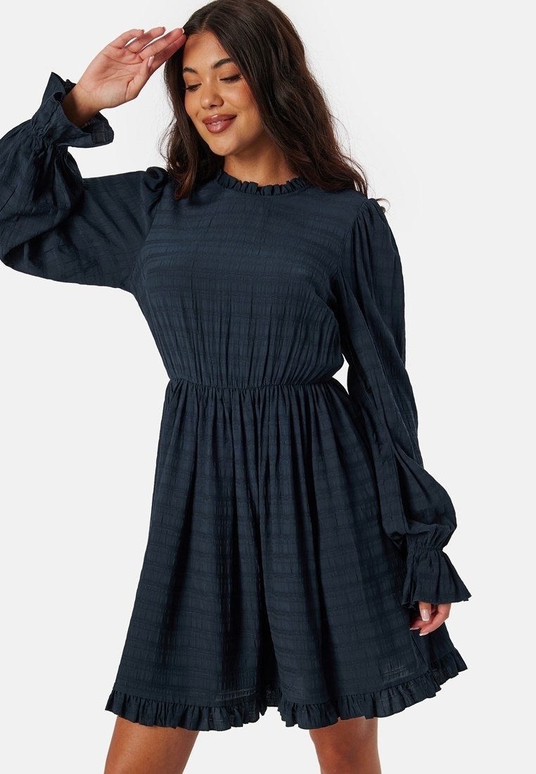 Robe texturée bleu marine avec de longues manches bouffantes et un ourlet froncé. Présente une taille ajustée et un col rond.
