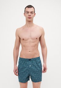 Boxer en turquoise à motif pour homme, fabriqué en tissu léger, avec une fermeture à bouton et une taille élastique ornée d'un imprimé discret.