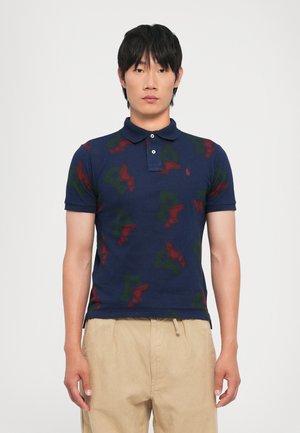 Navy polo shirt with green and red winged shoe and letter patterns, three-button placket, and short sleeves. Cotton fabric.
