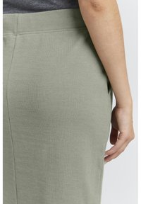 Fustă din material texturat, de culoare verde măsliniu, cu talie elastică. Prim-planul arată textura și finisajul neted, având o deschidere pe lateral vizibilă.