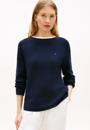 Πλεκτό πουλόβερ σε ναυτικό μπλε με μακριά μανίκια και στρογγυλή λαιμόκοψη, διακοσμημένο με μικρό λογότυπο στο στήθος και ριμπ μανσέτες και τελείωμα.