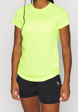 Neon gele sportshirt met korte mouwen en ronde hals; gecombineerd met zwarte shorts met een klein logo aan de zijkant. Gladde textuur.