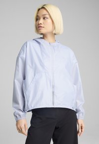 Veste à capuche légère de couleur violet clair en tissu lisse et léger. Elle dispose d'une fermeture éclair frontale, de poignets élastiques et de poches latérales.