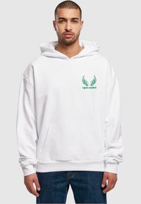 Weiße Kapuzenjacke mit Fronttasche, verziert mit gesticktem grünen Flügel-Logo. Weicher Stoff, lockere Passform und gerippte Bündchen und Saum.