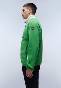 Green fleece jacket with a high white collar, zipper closure, and black accents. Features a logo patch on the left arm.