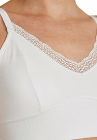Bralette bianco con scollatura a V, tessuto morbido e bordo decorativo in pizzo lungo i lati. Presenta spalline regolabili e una texture liscia.