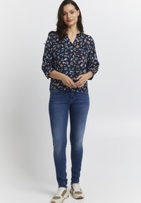 Blusa con motivo floreale di colore navy con maniche corte, abbinata a jeans skinny blu scuro e sneakers multicolori. Tessuto dalla trama liscia.