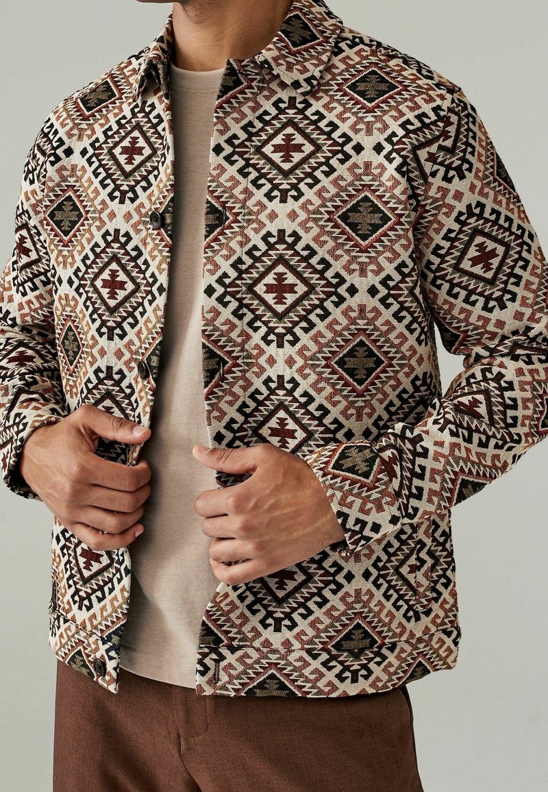 Camicia a pattern beige con disegni geometrici multicolore, dotata di apertura con bottoni, colletto e maniche lunghe. Vestibilità casual.