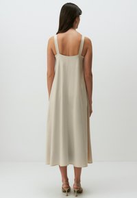 Abito midi beige con spalline sottili regolabili, vestibilità ampia e texture liscia che arriva giusto sopra le caviglie. Scarpe con tacco sottile.