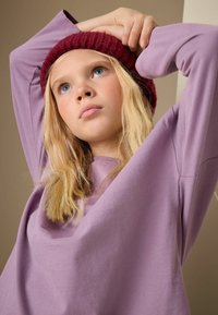 Purple long-sleeve shirt with a wide fit and soft texture, paired with a knitted burgundy beanie. The background is neutral.