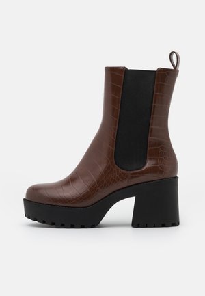 Bottine en cuir marron embossé crocodile avec panneau latéral élastique noir, talon plateforme noir épais, et languette à l'arrière.