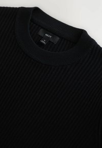 Schwarzer, gerippter Strickpullover mit Rundhalsausschnitt und einem Etikett, das "NEXT" in Weiß trägt. Der Stoff wirkt weich mit einer strukturierten Oberfläche.